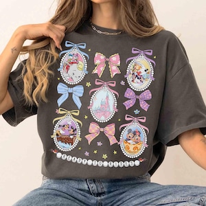 May include: A gray t-shirt with a graphic print of cartoon characters in oval frames. The frames are decorated with bows and flowers. The text "Ready for Rides" is printed at the bottom of the shirt.