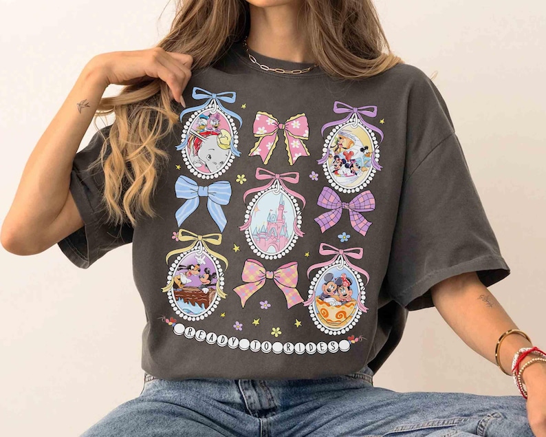 May include: A gray t-shirt with a graphic print of cartoon characters in oval frames. The frames are decorated with bows and flowers. The text "Ready for Rides" is printed at the bottom of the shirt.