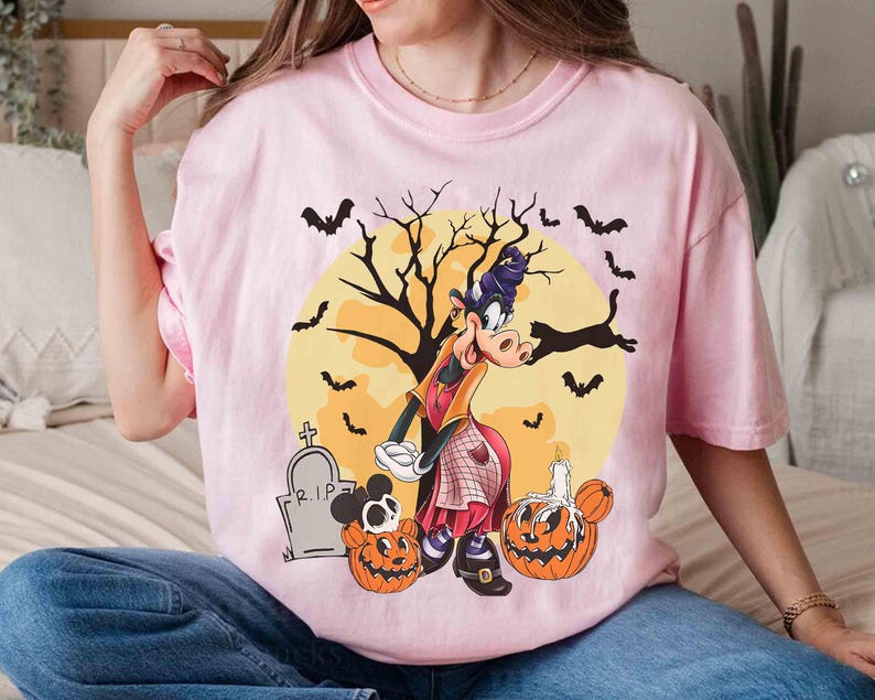 Peut inclure: T-shirt rose clair avec un motif d'Halloween. Le motif comprend un personnage de dessin anim&eacute; d&eacute;guis&eacute; en sorci&egrave;re, des chauves-souris, des citrouilles, une pierre tombale et une pleine lune. Le t-shirt est de style d&eacute;contract&eacute; &agrave; manches courtes.