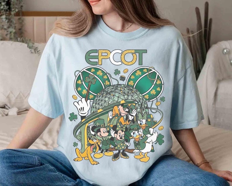 May include: Light blue t-shirt featuring a graphic of Disney characters celebrating St. Patrick's Day at Epcot. The design includes Mickey, Minnie, Donald, Daisy, Goofy, and Pluto, with shamrocks and the Epcot logo.