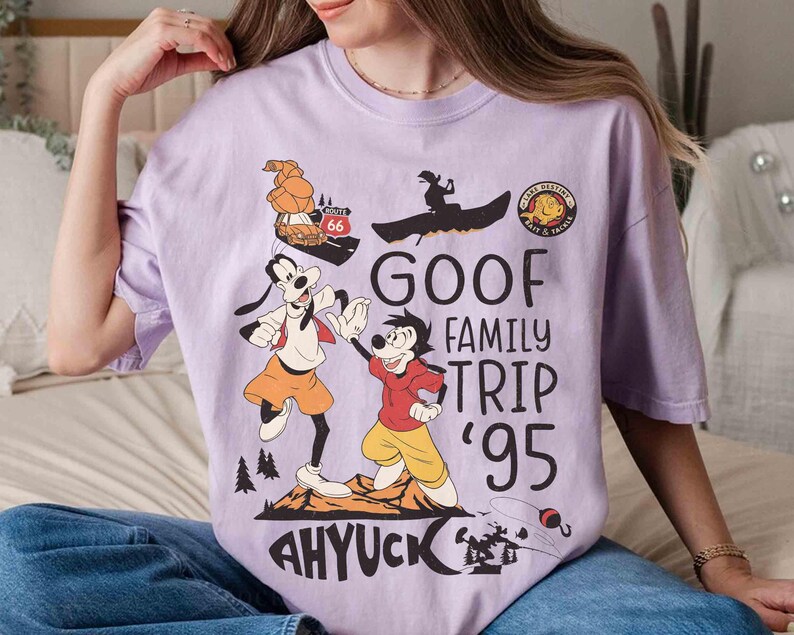 Pode incluir: Camiseta lil&aacute;s clara com um desenho do Pateta e Max do filme "Pateta e Max". O design inclui o texto "Goof Family Trip '95" e "Ahyuck!" com elementos de desenho animado.