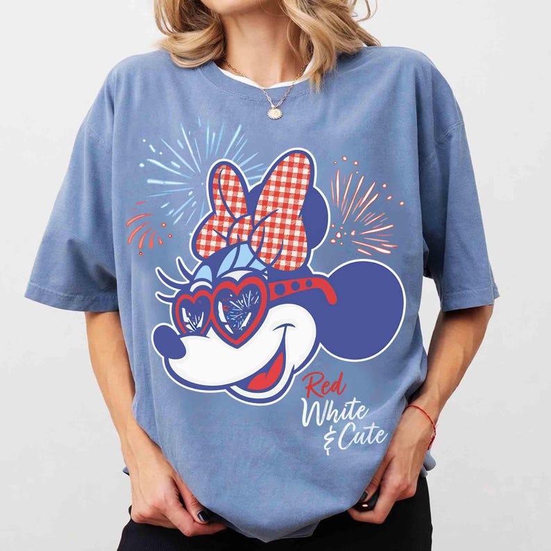 Op de afbeelding: Lichtblauw T-shirt met een cartoon muis ontwerp. De muis heeft een rood-witte ruitjesstrik, hartvormige zonnebril en vuurwerk. De tekst "Red White & Cute" is cursief geschreven. Het T-shirt heeft korte mouwen.