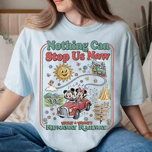 Peut inclure: T-shirt bleu clair avec un motif color&eacute;. Le motif comprend le texte "Nothing Can Stop Us Now", un soleil de dessin anim&eacute;, un train et une voiture rouge avec Mickey et Minnie Mouse. Le t-shirt est de coupe ample.