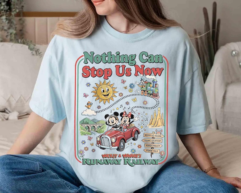 Peut inclure: T-shirt bleu clair avec un motif color&eacute;. Le motif comprend le texte "Nothing Can Stop Us Now", un soleil de dessin anim&eacute;, un train et une voiture rouge avec Mickey et Minnie Mouse. Le t-shirt est de coupe ample.