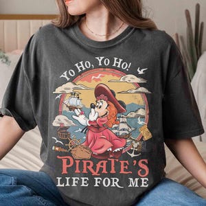 May include: Dark gray t-shirt featuring a cartoon pirate mouse character in a red dress and hat, with the text "Yo Ho, Yo Ho! Pirate's Life For Me." The design includes a ship, treasure chest, and seagulls, set within a circular frame.