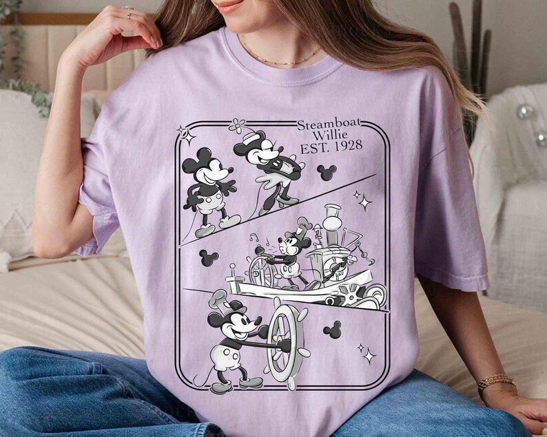 Może przedstawiać: Jasnofioletowa koszulka z czarno-białą grafiką Myszki Miki ze Steamboat Willie. Grafika przedstawia Myszkę Miki w r&oacute;żnych pozach, napis "Steamboat Willie EST. 1928" i sylwetki Myszki Miki.