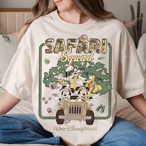May include: A cream-coloured t-shirt with a graphic of Disney characters in a safari jeep. The design includes the text "SAFARI Squad" and "Walt Disney World". The jeep is surrounded by cartoon trees and paw prints.