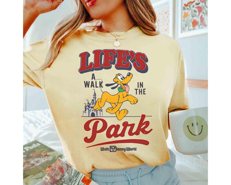 May include: Yellow t-shirt with the text "LIFE'S A WALK IN THE PARK" in red and blue, featuring a cartoon Pluto character and a castle graphic. The shirt also has the "Walt Disney World" logo.