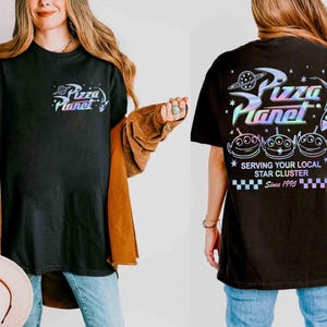 May include: Black t-shirt with a colorful "Pizza Planet" logo and alien graphic. The shirt features the text "Serving Your Local Star Cluster Since 1995" on the back. A fun, casual tee.