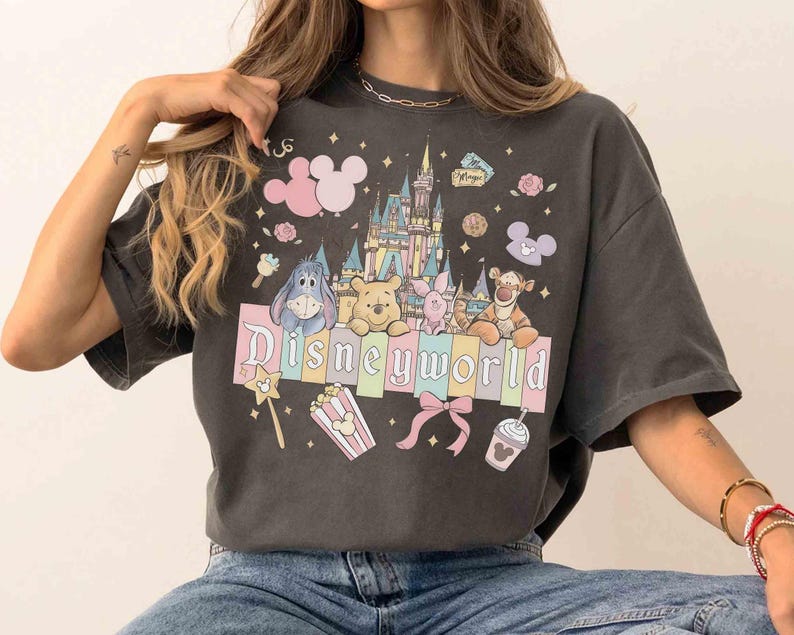 May include: Dark gray t-shirt featuring a colorful Disney World graphic. The design includes the Disney World castle, Mickey Mouse ears, and various Disney characters. The text "Disneyworld" is prominently displayed across the front.