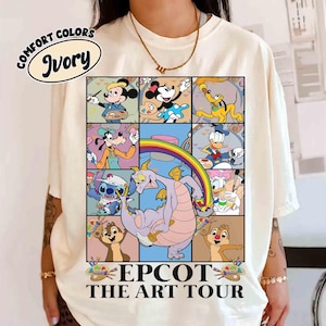 May include: Ivory-colored t-shirt featuring a colorful graphic of Disney characters in a grid, including Mickey Mouse, Minnie Mouse, Pluto, Goofy, Donald Duck, Stitch, Chip and Dale, and Figment. The text "EPCOT THE ART TOUR" is printed below the grid.