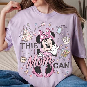 K&ouml;nnte beinhalten: Helllila T-Shirt mit Minnie Mouse und dem Text "THIS MOM CAN". Das Design beinhaltet einen Einkaufswagen, ein Telefon, eine To-Do-Liste und andere Symbole. Das Shirt ist ein l&auml;ssiger Stil.