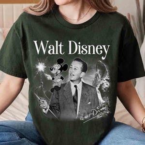 Puede incluir: Una camiseta de manga corta de color verde oscuro con un estampado gr&aacute;fico de Walt Disney y Mickey Mouse. El dise&ntilde;o incluye el texto Walt Disney en la parte superior, una imagen en blanco y negro de Walt Disney, una peque&ntilde;a figura de Mickey y una firma.