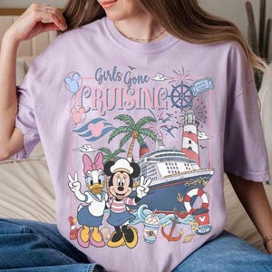 Peut inclure: T-shirt lilas clair avec l'inscription "Girls Gone Cruising" et un motif avec Daisy Duck et Minnie Mouse. Le motif comprend un bateau de croisi&egrave;re, un phare, des palmiers et des &eacute;l&eacute;ments nautiques. Le t-shirt est de coupe ample.