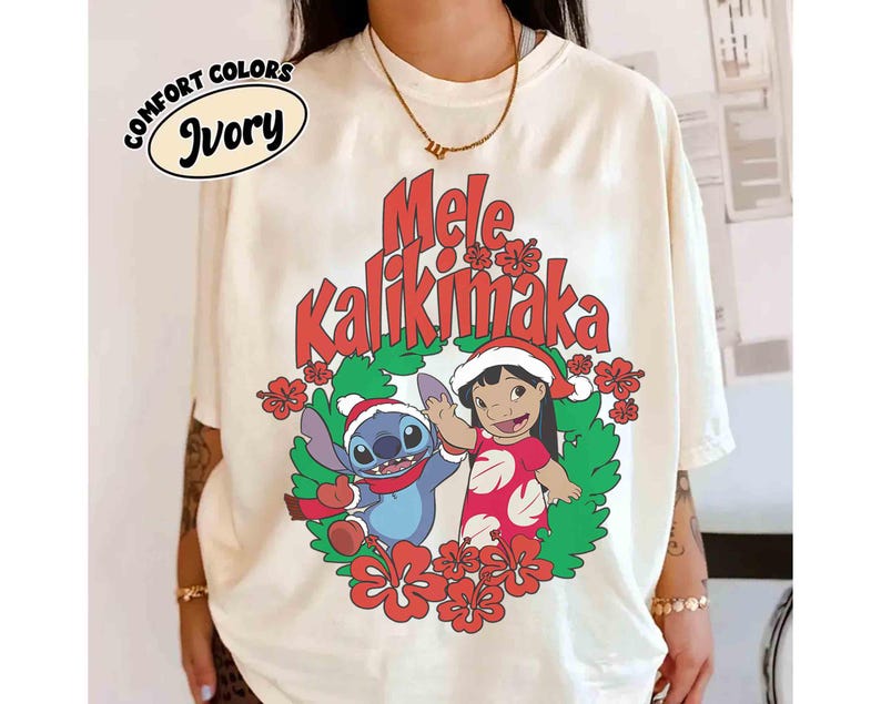 May include: Ivory-colored Comfort Colors t-shirt featuring a festive design. The graphic includes the text "Mele Kalikimaka" in red, along with cartoon characters Stitch and Lilo in Santa hats, surrounded by a wreath of flowers.