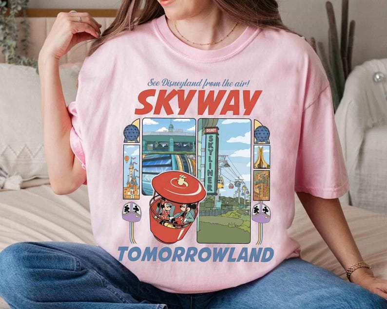 Puede incluir: Camiseta rosa claro con un dise&ntilde;o gr&aacute;fico que presenta las palabras "SKYWAY" y "TOMORROWLAND". El dise&ntilde;o incluye una g&oacute;ndola roja con Mickey y Minnie Mouse, e im&aacute;genes de las atracciones de Disneyland. La camiseta tiene cuello redondo y mangas cortas.