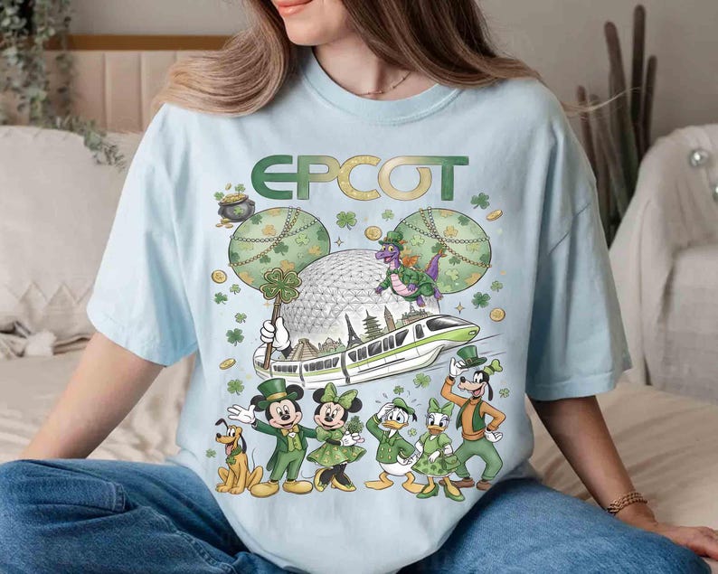 May include: Pale blue t-shirt with a green "EPCOT" logo and a St. Patrick's Day themed Disney graphic. The design includes Mickey and Minnie Mouse, Donald Duck, Goofy, and a dragon, with a monorail and the EPCOT sphere.