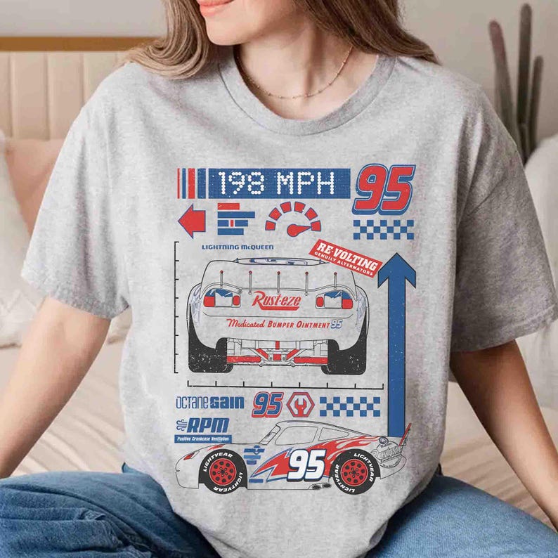 K&ouml;nnte beinhalten: Ein graues, meliertes T-Shirt mit einem Grafikdruck eines Rennwagens in R&uuml;ck- und Seitenansicht. Das Design enth&auml;lt den Text 198 MPH, 95, Rust-eze, Lightning McQueen, Re-volting, Octane Gain und RPM sowie verschiedene Rennsport-Symbole.