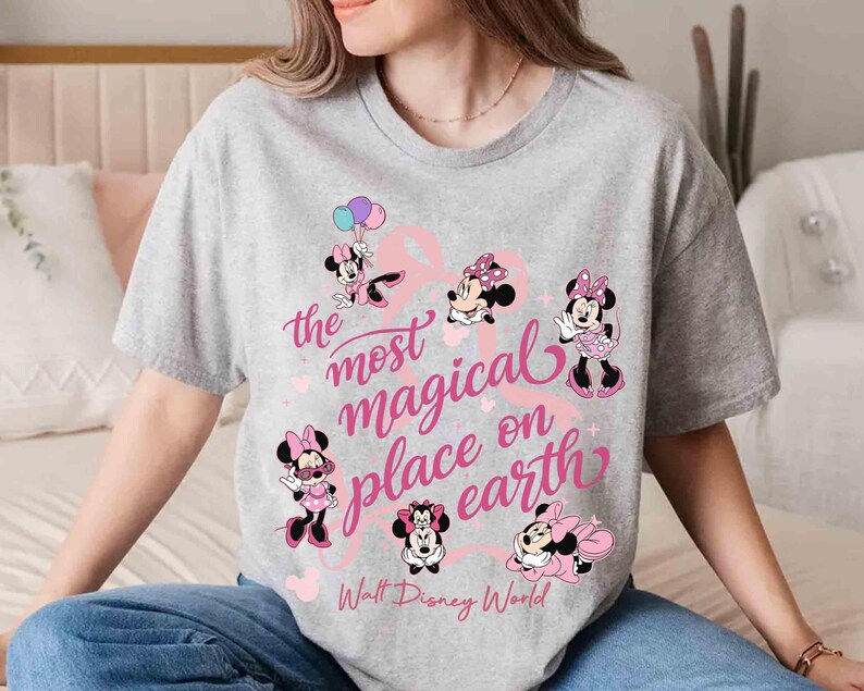 K&ouml;nnte beinhalten: Ein graues T-Shirt mit mehreren Minnie-Maus-Illustrationen in Rosa und Schwarz. Der Text "the most magical place on earth" ist in rosa Schrift geschrieben, darunter "Walt Disney World".