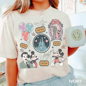 Peut inclure: T-shirt ivoire avec un motif sur le th&egrave;me de Disney. Le graphisme comprend Mickey Mouse, un ch&acirc;teau, des ballons et des billets de parc. Les mots "Walt Disney" et "Mickey Mouse" sont &eacute;galement pr&eacute;sents. Le t-shirt est &agrave; col rond et &agrave; manches courtes.