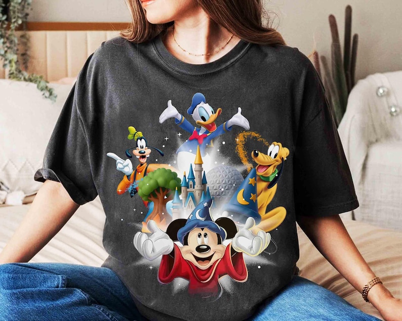 May include: Dark gray t-shirt featuring a colorful graphic of Disney characters Mickey Mouse, Donald Duck, Goofy, and Pluto, with a castle and a sphere in the background. The design has a vintage, distressed look.