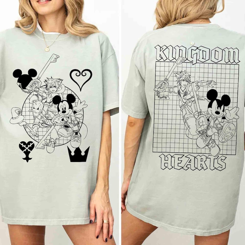 Puede incluir: Camiseta verde claro con un gr&aacute;fico en blanco y negro de Mickey Mouse y otros personajes con armas en forma de llave. La parte trasera de la camiseta tiene las palabras "Kingdom Hearts".