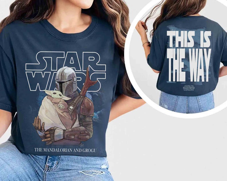 May include: A navy blue t-shirt featuring a Star Wars graphic on the front with The Mandalorian holding Grogu and the text The Mandalorian and Grogu. The back of the shirt displays the white text This Is The Way with a Star Wars logo below it.