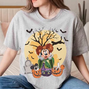 Peut inclure: T-shirt gris clair avec un motif d'Halloween. Le motif pr&eacute;sente un personnage de dessin anim&eacute; aux cheveux roux, une cape verte et une robe violette, sur fond de lune jaune, de chauves-souris et de citrouilles. Une pierre tombale avec "R.I.P." est &eacute;galement visible.