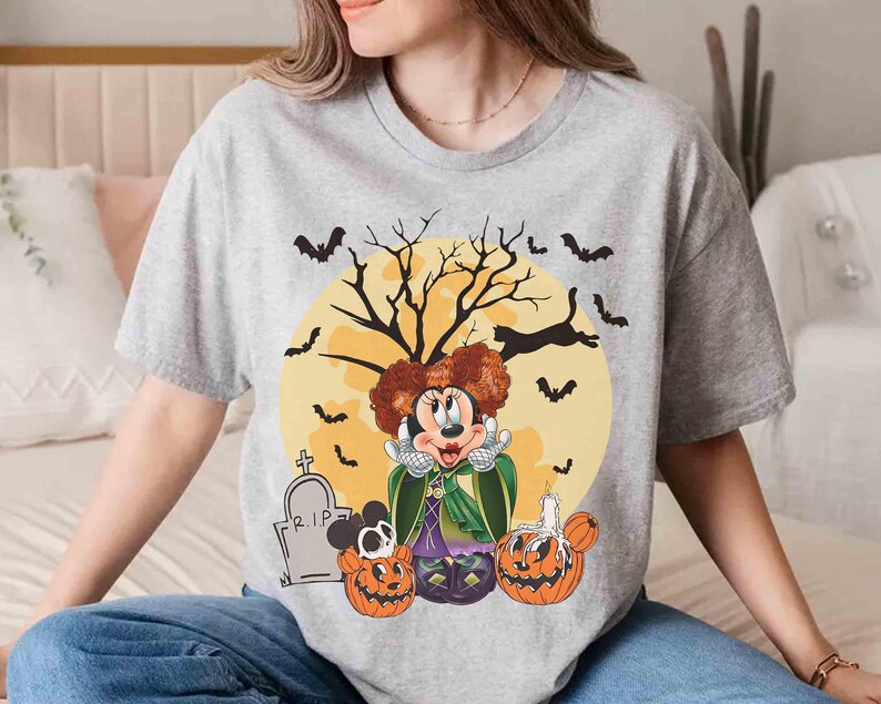 Peut inclure: T-shirt gris clair avec un motif d'Halloween. Le motif pr&eacute;sente un personnage de dessin anim&eacute; aux cheveux roux, une cape verte et une robe violette, sur fond de lune jaune, de chauves-souris et de citrouilles. Une pierre tombale avec "R.I.P." est &eacute;galement visible.