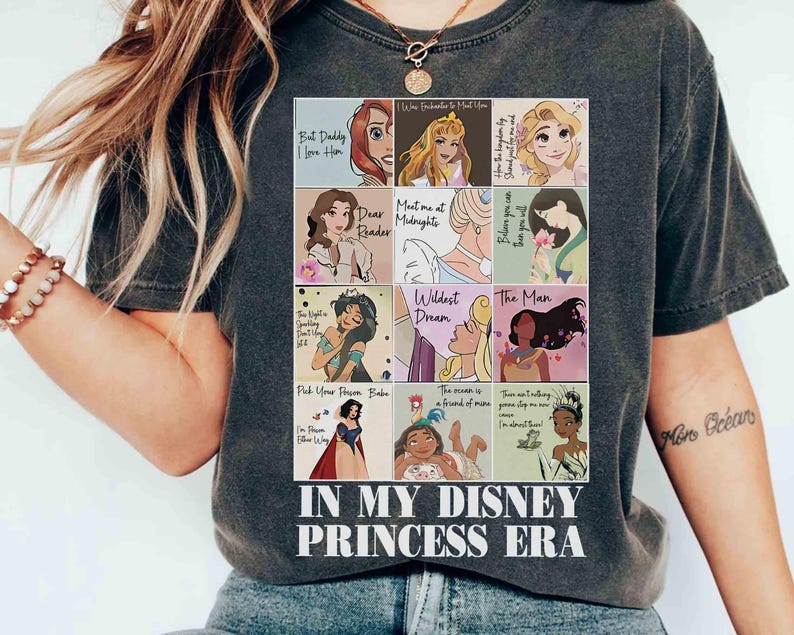 May include: Dark gray t-shirt featuring a collage of Disney Princess illustrations with quotes. The shirt includes the text "IN MY DISNEY PRINCESS ERA" in a white, bold font. The shirt is a casual wear item.