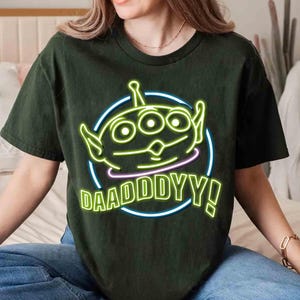 May include: A dark green t-shirt with a neon green alien character and the text "DAADDY!" in a neon green circle.
