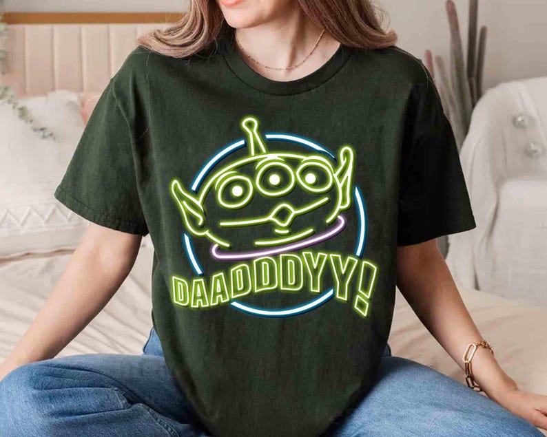May include: A dark green t-shirt with a neon green alien character and the text "DAADDY!" in a neon green circle.