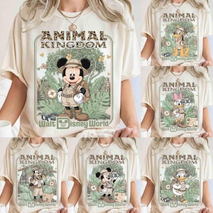 Puede incluir: Camisetas color crema con varios personajes de Disney con trajes de safari, con el texto "ANIMAL KINGDOM" y "Walt Disney World". Mickey Mouse, Pluto, Daisy, Donald y Goofy se representan en un entorno selv&aacute;tico.