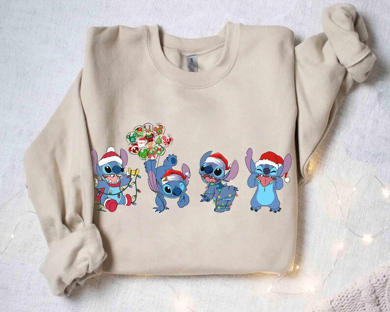 Puede incluir: Sudadera beige con cuatro personajes de dibujos animados azules, cada uno con un gorro de Pap&aacute; Noel. Los personajes est&aacute;n en varias poses, algunos sosteniendo luces navide&ntilde;as y adornos. Un dise&ntilde;o festivo y colorido para la temporada navide&ntilde;a.