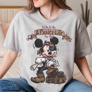 Puede incluir: Una camiseta gris con una imagen de dibujos animados de Mickey Mouse vestido de pirata. El texto "Yo Ho, Yo Ho, A Pirates Life For Me!" est&aacute; impreso en la camiseta.