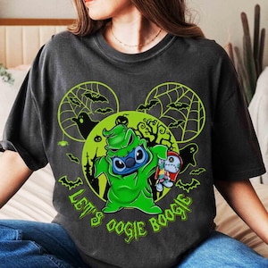 以下が含まれることがあります： 「Let's Oogie Boogie」の文字と、緑色のコスチュームを着た緑色の漫画のキャラクターが描かれた、濃いグレーのTシャツ。デザインには、コウモリ、クモの巣、緑色の月が含まれています。