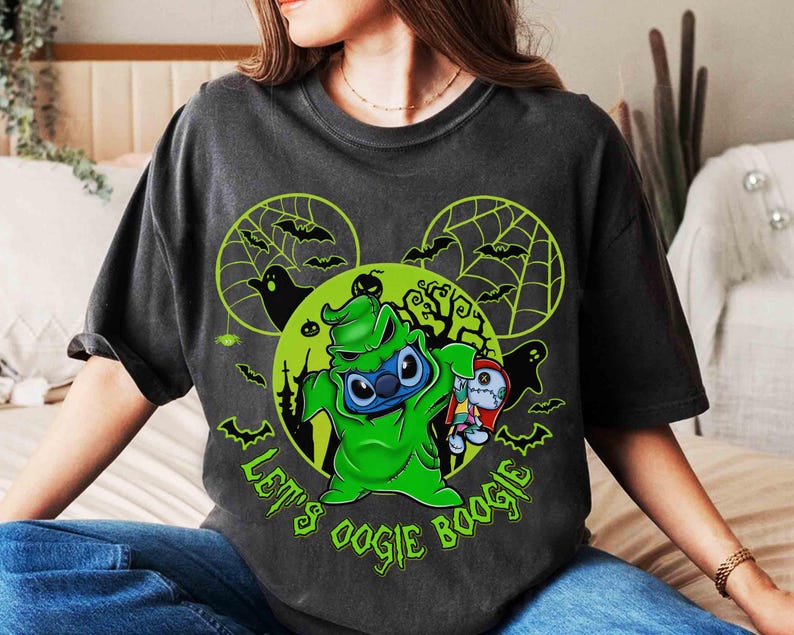 May include: Dark gray t-shirt featuring a green cartoon character in a green costume with the text "Let's Oogie Boogie". The design includes bats, spiderwebs, and a green moon.