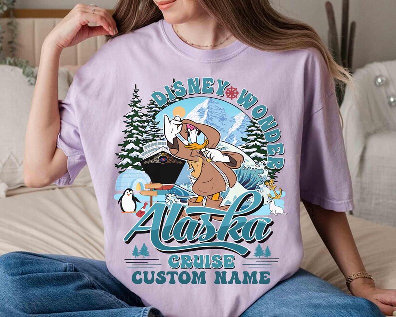 May include: A light purple t-shirt featuring a graphic of Donald Duck in a brown coat, with the text "Disney Wonder Alaska Cruise Custom Name". The design includes a cruise ship, mountains, and a penguin.