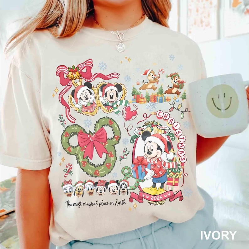 May include: Ivory-colored t-shirt featuring a festive Christmas design with Mickey Mouse, Minnie Mouse, Chip and Dale, and other Disney characters. The shirt includes the text "Very Merry Christmas" and "The most magical place on Earth."