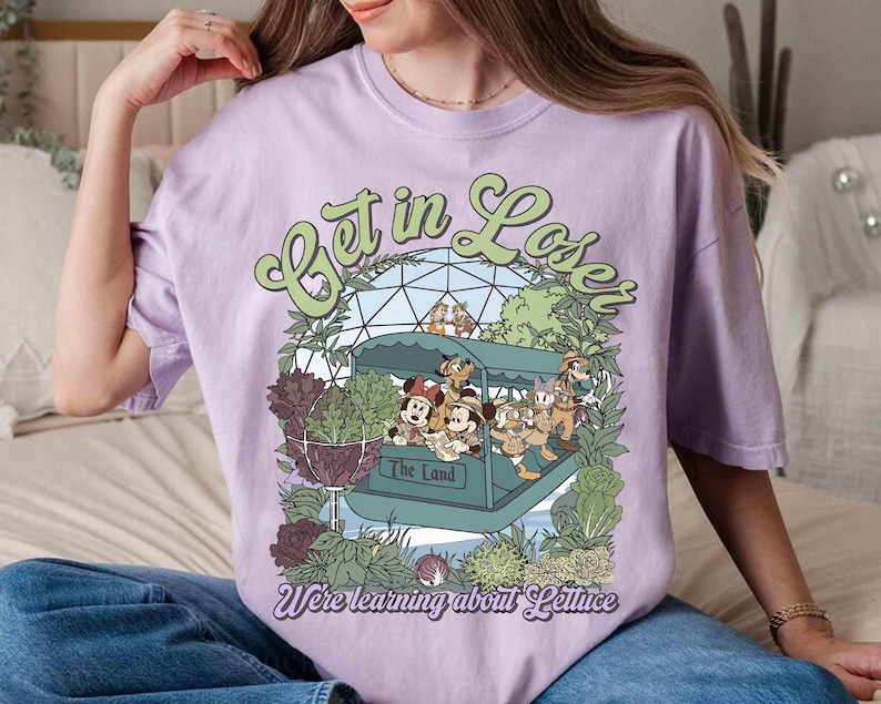 May include: A light purple t-shirt featuring a cartoon graphic of a boat with Disney characters and the text "Get in Loser, We're learning about Lettuce". The shirt has a crew neck and short sleeves.