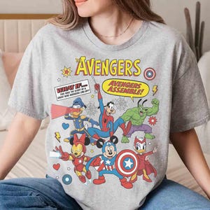 May include: A grey t-shirt with a comic book style design. The design features the text "The Avengers" and "Avengers Assemble!" alongside cartoon versions of Marvel characters such as Spider-Man and Hulk, and Disney characters.