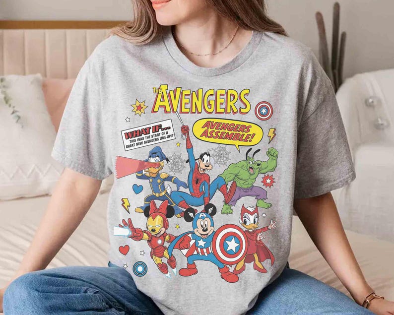 May include: A grey t-shirt with a comic book style design. The design features the text "The Avengers" and "Avengers Assemble!" alongside cartoon versions of Marvel characters such as Spider-Man and Hulk, and Disney characters.