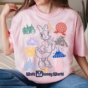 Może przedstawiać: Jasnor&oacute;żowa koszulka z grafiką Daisy Duck i r&oacute;żnymi ikonami Disney World. Koszulka zawiera czarny napis "Walt Disney World". Projekt zawiera kolorowe ilustracje kultowych atrakcji parku.