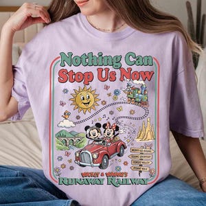 Peut inclure: T-shirt lilas avec un motif color&eacute; repr&eacute;sentant Mickey et Minnie Mouse dans une voiture rouge, un train et un soleil souriant. Le texte "Nothing Can Stop Us Now" et "Runaway Railway" est &eacute;galement affich&eacute;.