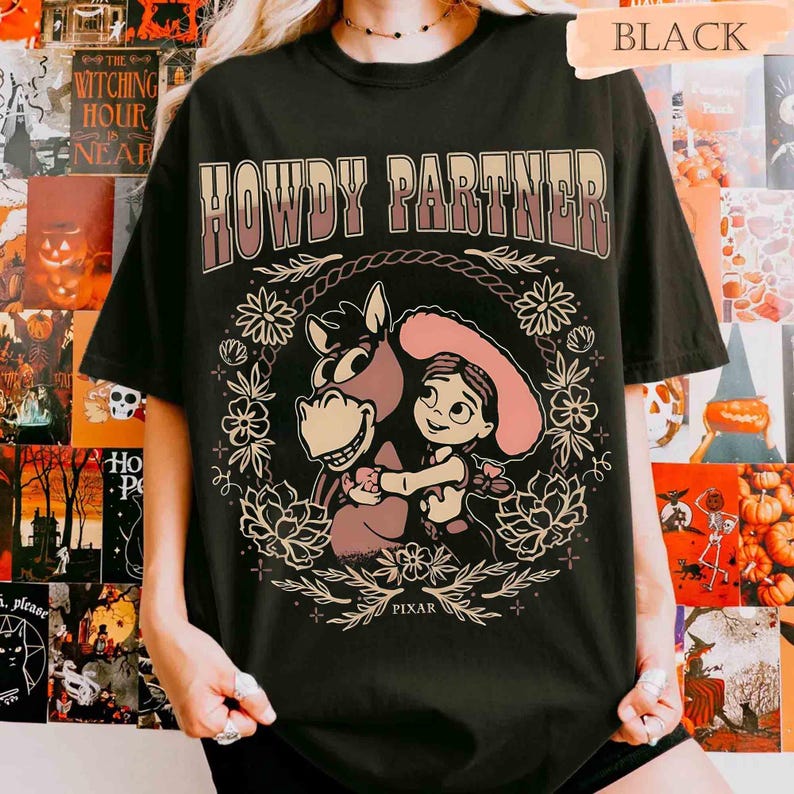 Puede incluir: Una camiseta negra de manga corta con el texto HOWDY PARTNER en una fuente degradada sobre un gr&aacute;fico de una vaquera de dibujos animados abrazando a un caballo. El dise&ntilde;o est&aacute; rodeado por una corona floral e incluye la palabra PIXAR abajo.