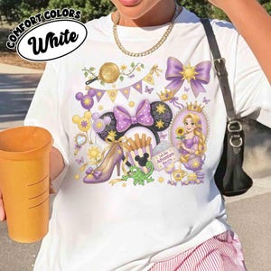 May include: White t-shirt with a colorful graphic featuring a princess, Minnie Mouse ears, a high heel, and the text "Let the Adventure Begin." The design incorporates purple, yellow, and gold elements.