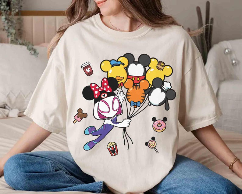 Puede incluir: Camiseta color crema con un personaje de dibujos animados sosteniendo globos con forma de personajes de Disney. El dise&ntilde;o incluye una taza de caf&eacute;, helado, palomitas de ma&iacute;z, una rosquilla y una piruleta. La camiseta es holgada.