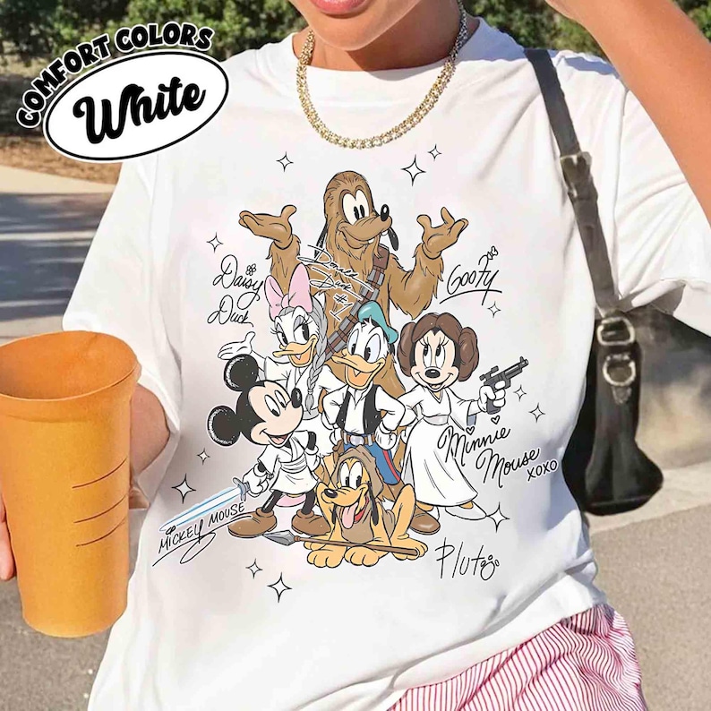 May include: White t-shirt with a graphic featuring Disney characters in Star Wars-themed costumes. The shirt includes the text "COMFORT COLORS" and "White" in a circular design. Character names and signatures are also present.