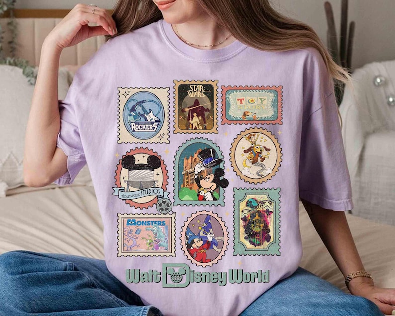 Puede incluir: Una camiseta de color lila claro con varios dise&ntilde;os de sellos postales con tem&aacute;tica de Disney. Los sellos muestran personajes y logotipos de pel&iacute;culas y atracciones de Disney, incluyendo "Star Wars" y "Hollywood Studios". El texto "Walt Disney World" est&aacute; en la parte inferior.