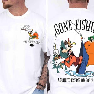 May include: White t-shirt featuring a cartoon illustration of Goofy fishing. The front of the shirt has a small graphic with the text "THE PERFECT CAST". The back of the shirt has a larger graphic with the text "GONE FISHING" and "A GUIDE TO FISHING THE GOOFY WAY".